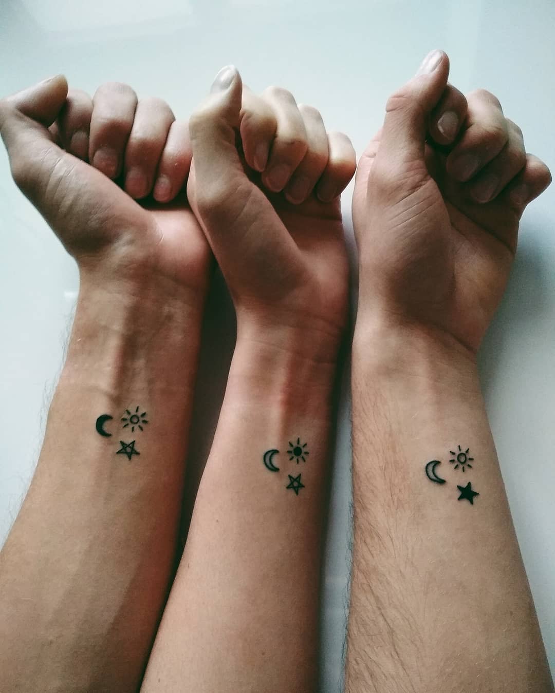 Matching wrist tattoos with a crescent moon, sun, and star, symbolizing unity and balance between night and day